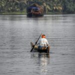 A serene view of a person rowing a wooden canoe in Kerala's picturesque backwaters.