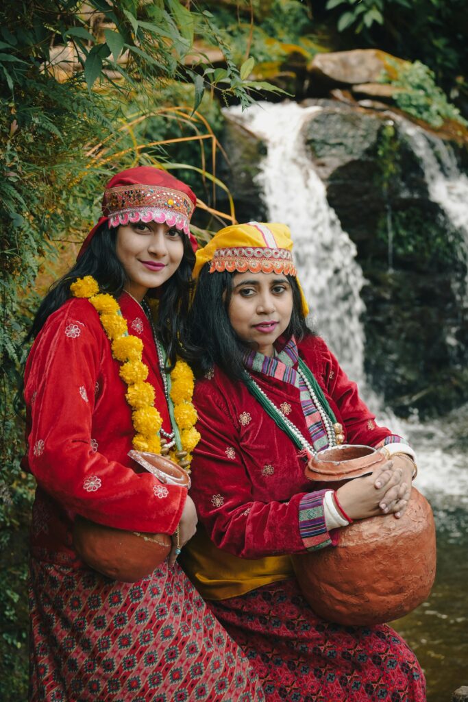Two women in traditional attire by a waterfall in Darjeeling, India, showcasing cultural heritage.