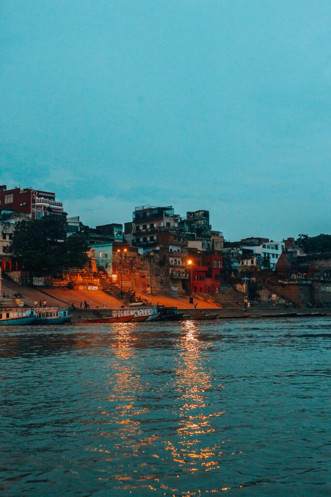 Scenic dusk view of Varanasi waterfront, featuring buildings and reflections on the Ganges River.